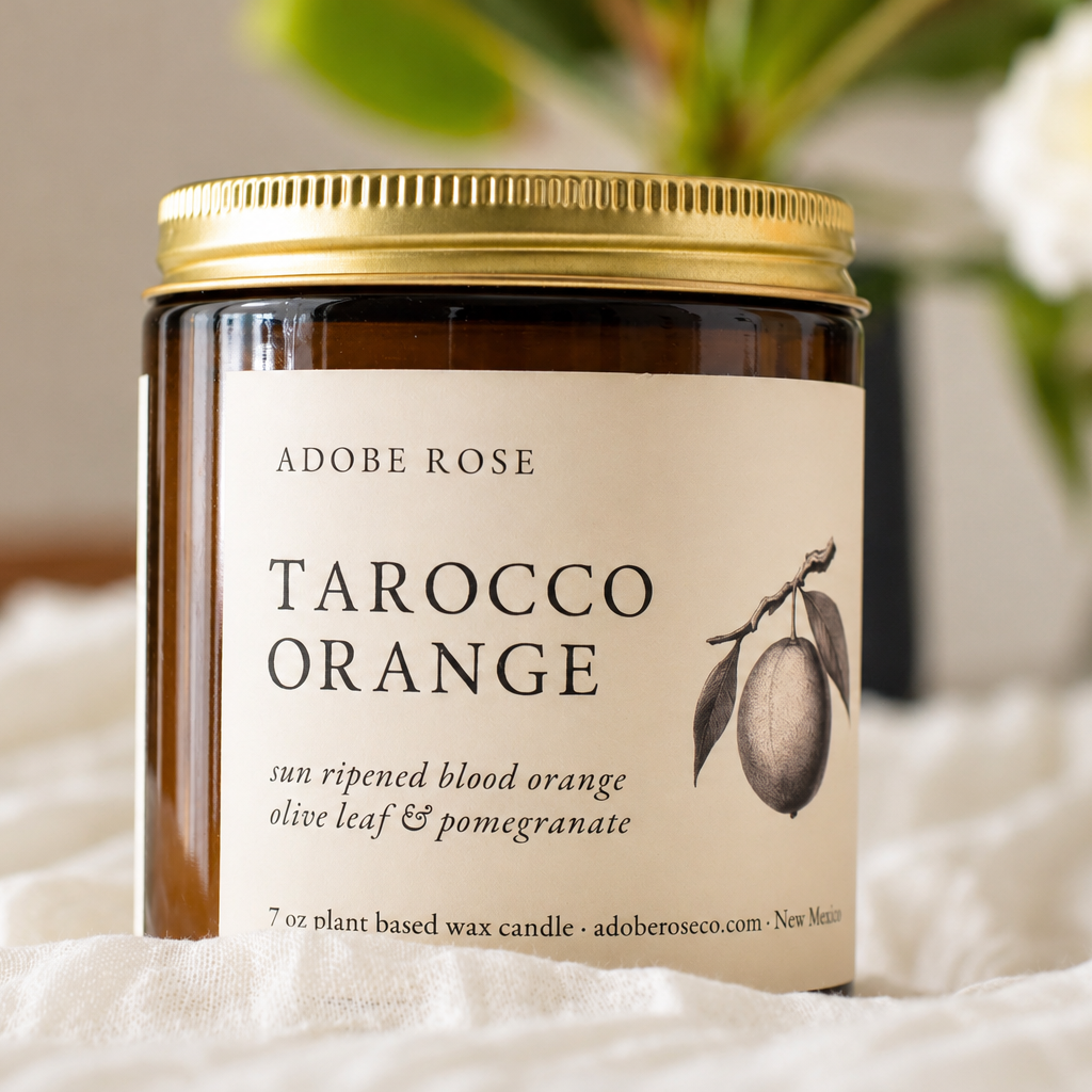 Jar of Adobe Rose Tarocco Orange candle on a soft surface with a blurred background