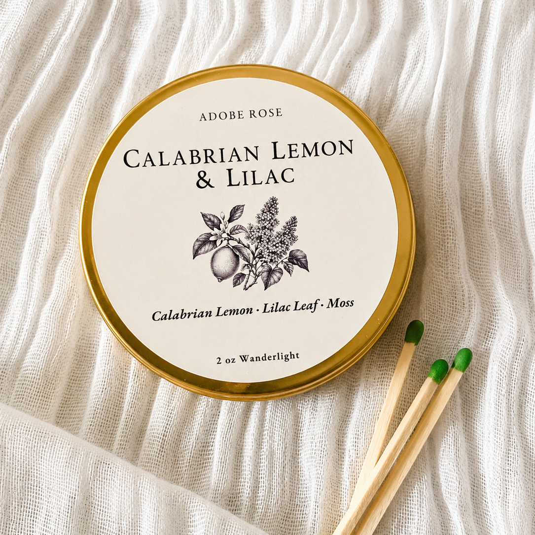 Tin of Adobe Rose Calabrian Lemon & Lilac candle on a textured fabric background