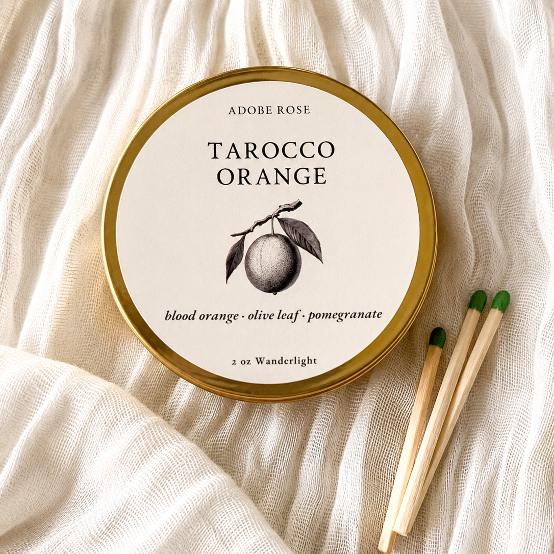 Adobe Rose Tarocco Orange candle on a textured white fabric background
