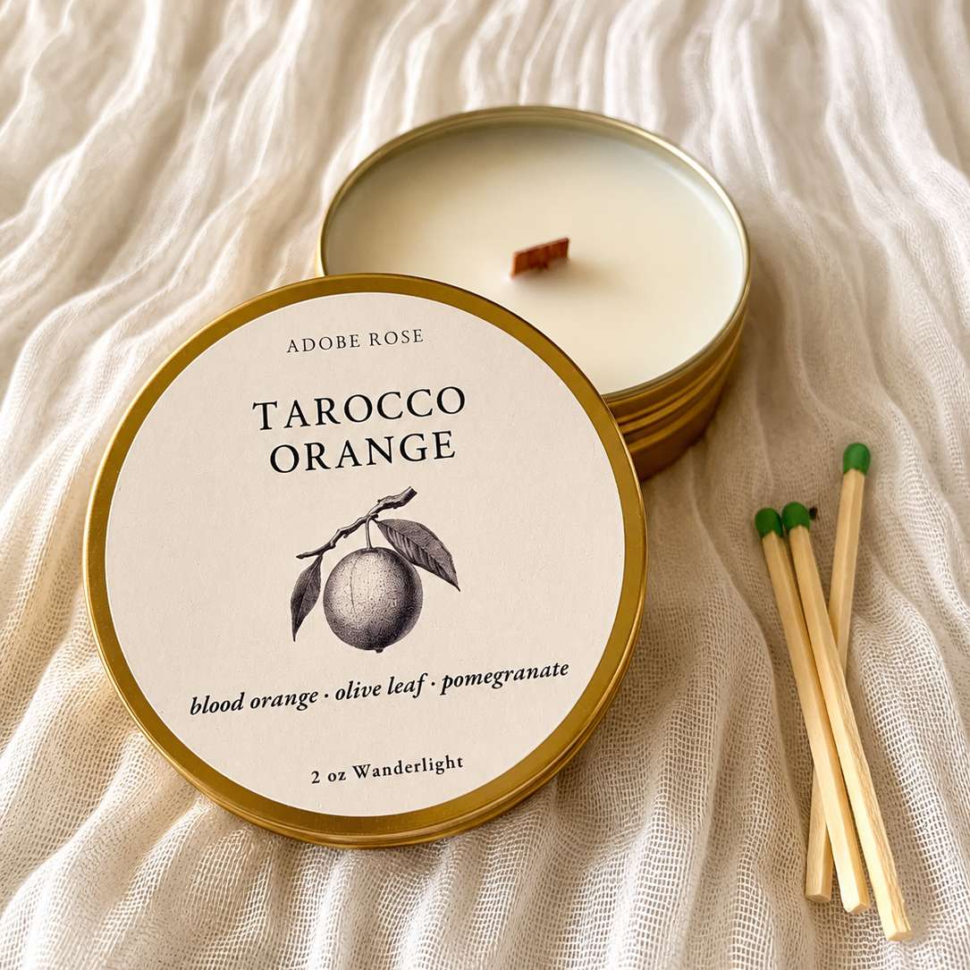 Wax candle in a metal tin labeled 'Tarocco Orange' on a textured fabric background