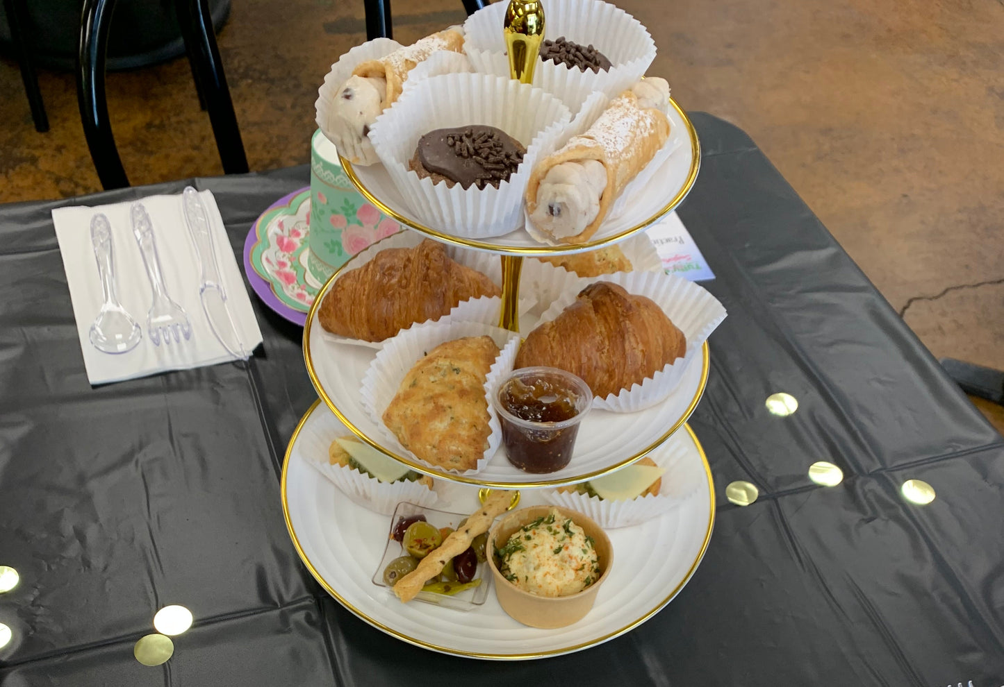High tea set with pastries and teacup on a black tray with a menu and silverware.